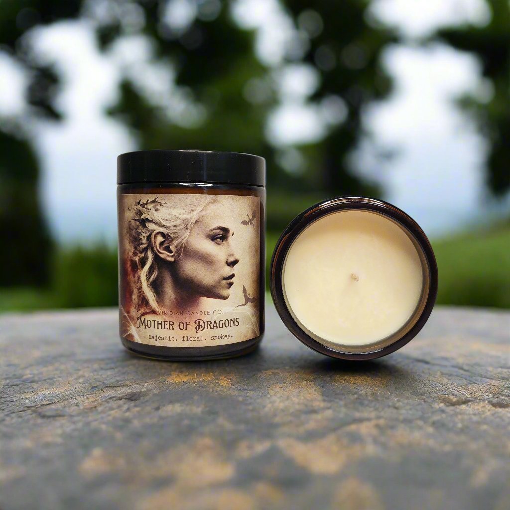 Mother of Dragons Soy fantasy candle, handcrafted by Viridian Candle Co. Candle is on a stone surface with a forest in the background. A second candle showing the inside cotton wick.