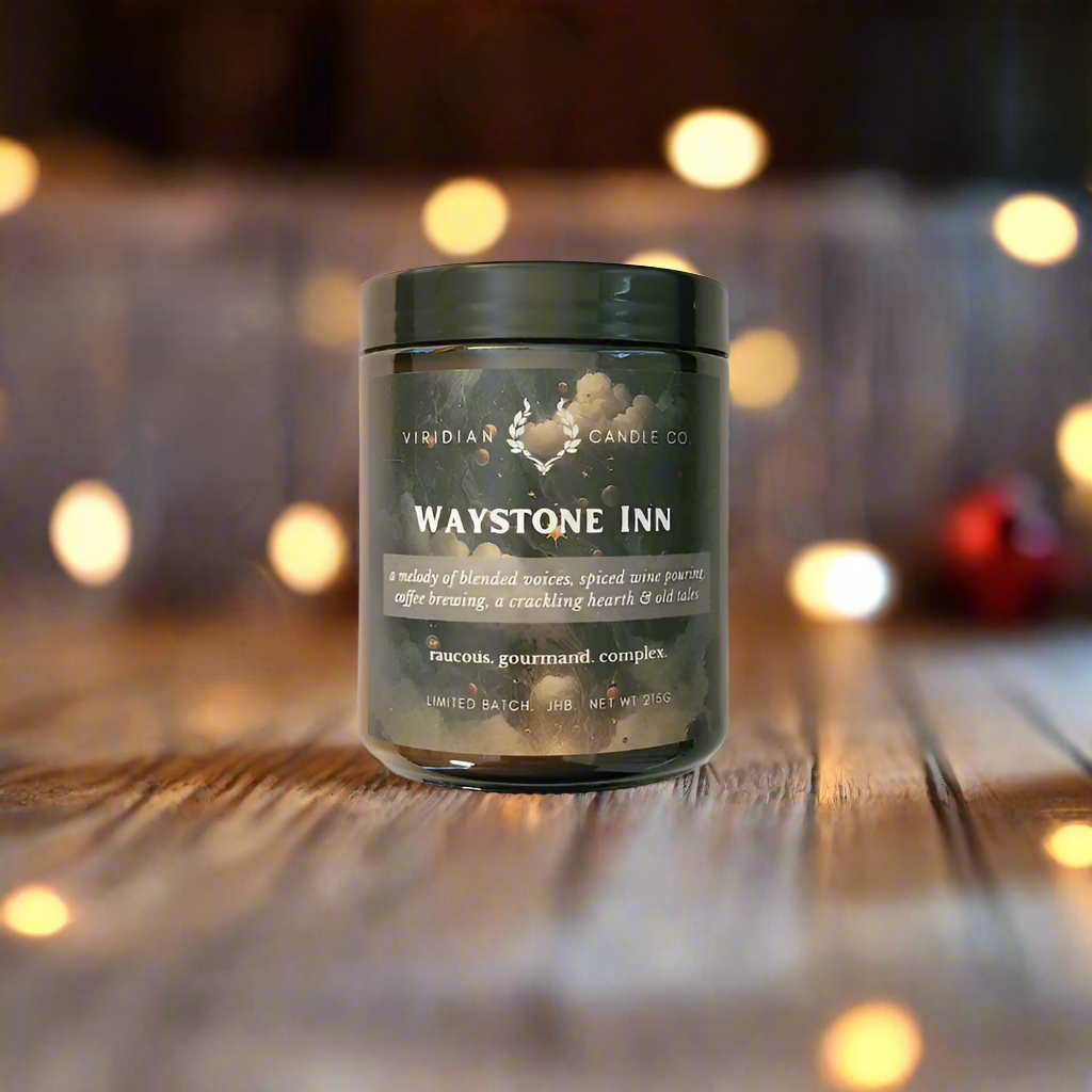 A Waystone Inn soy fantasy candle inspired by the scent of fantasy taverns and inns, handcrafted by Viridian Candle Co. The candle is placed on a wooden surface with a blurred background.