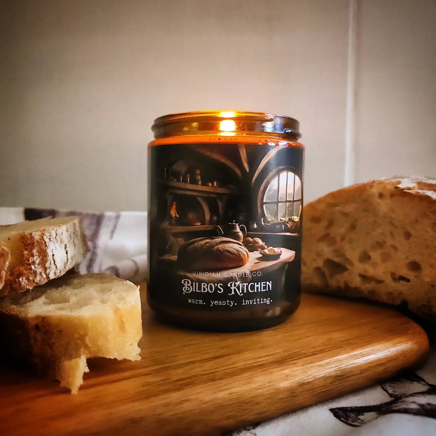 Most Loved Candles - a Bilbo's Kitchen fantasy candle on a wooden board with slabs of freshly baked bread  around - handcrafted by Viridian Candle Co.