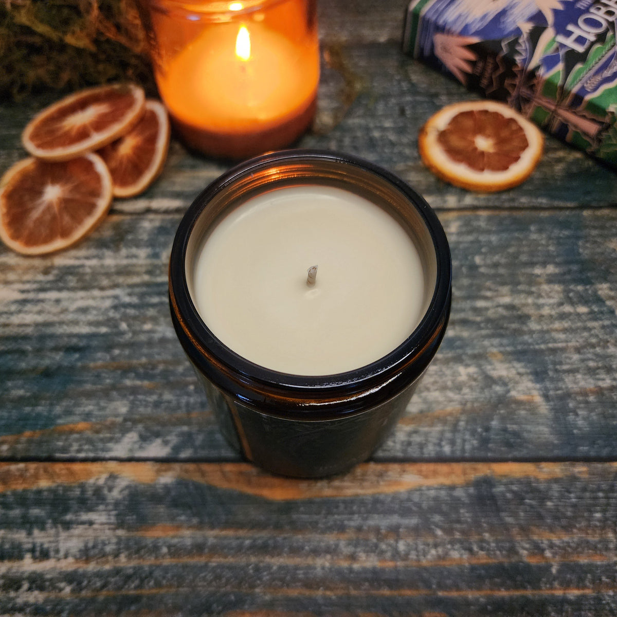 Candle in a black container on a wooden surface with dried oranges and another candle in the background.