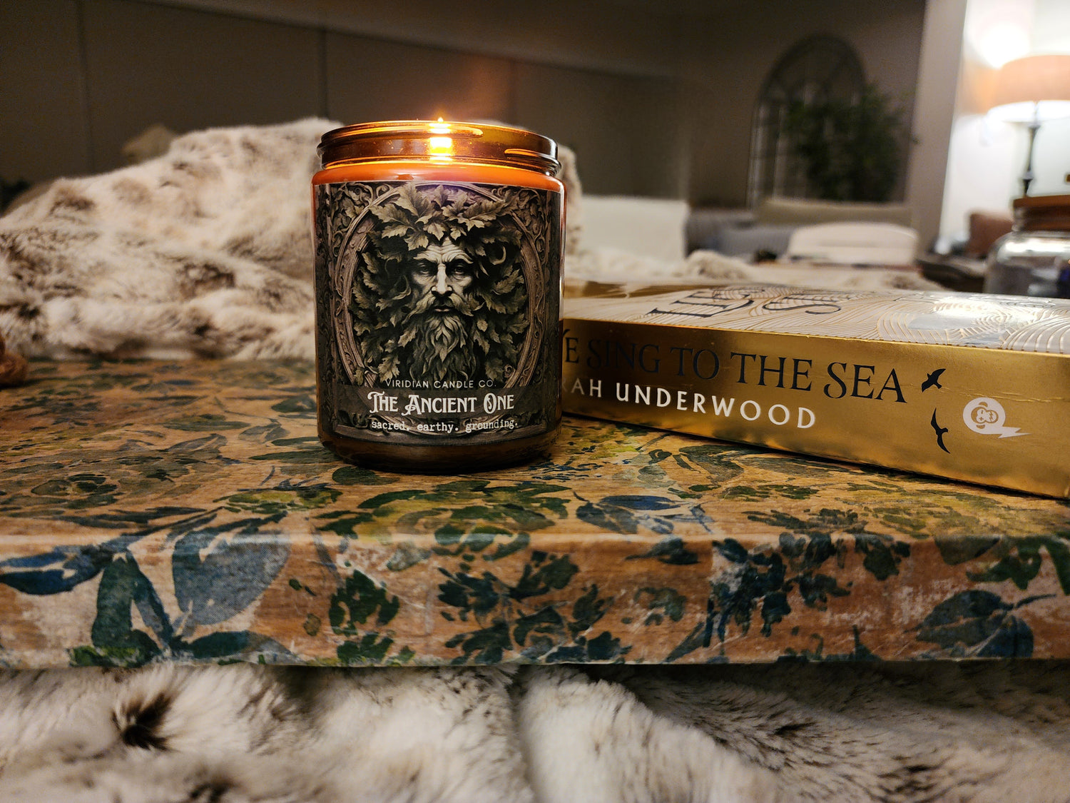 Ancient One fantasy candle created by Viridian Crafts on a vintage surface with faux furs and a book.