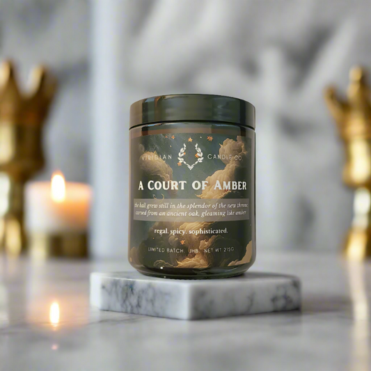 A soy fantasy candle labelled 'A Court of Amber' on a marble slab on a luminous counter with accents of gold and ambient lighting