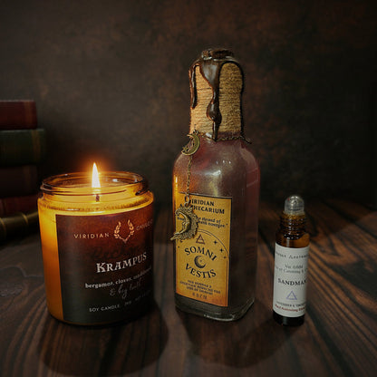 Alchemist’s Ritual dark academia bundle featuring a lit Krampus artisan fantasy candle, Dream Veil potion bottle, and Sandman fragrance essence on a dark wooden surface.