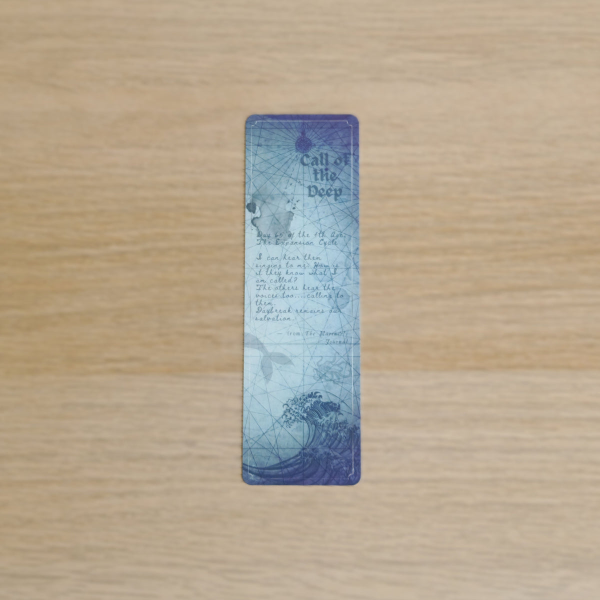 A rectangular vintage-style bookmark  'Call of the Deep' wave illustration and text, displayed vertically on a light wood grain background.