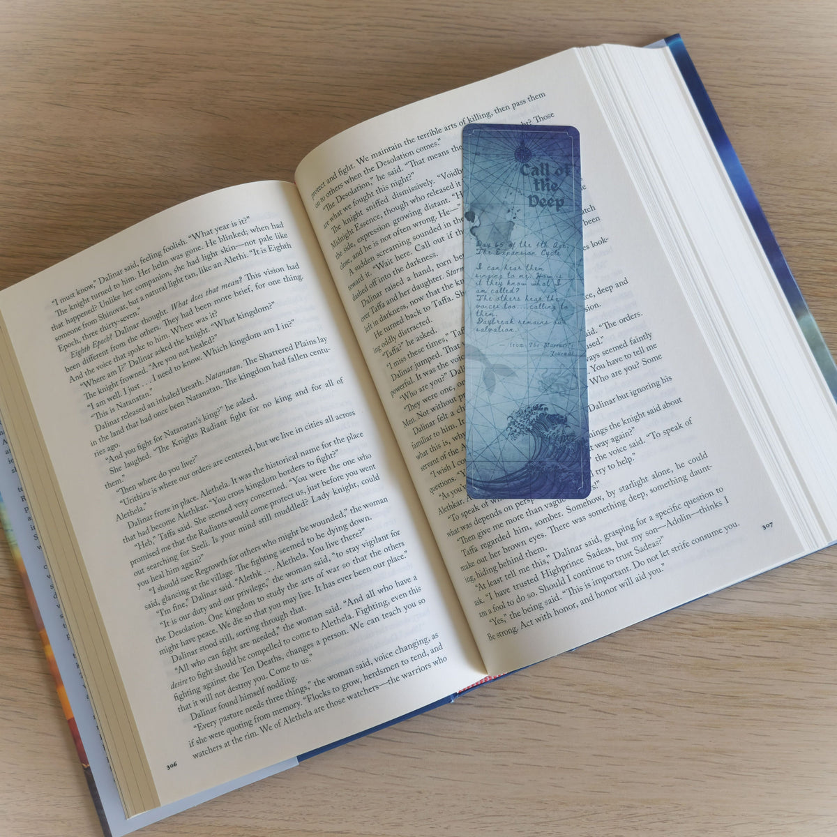 A decorative blue bookmark with a vintage map design and the text 'Call of the Deep' is placed on an open book with printed pages, photographed on a light wood surface.