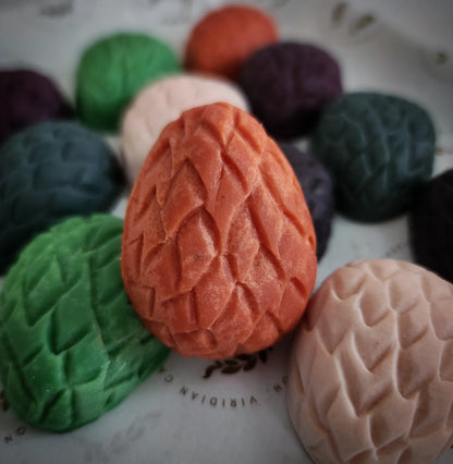 A collection of shimmery, multicolored dragon egg wax truffles, with varying shades including green, purple, orange, and beige, displayed on a surface.