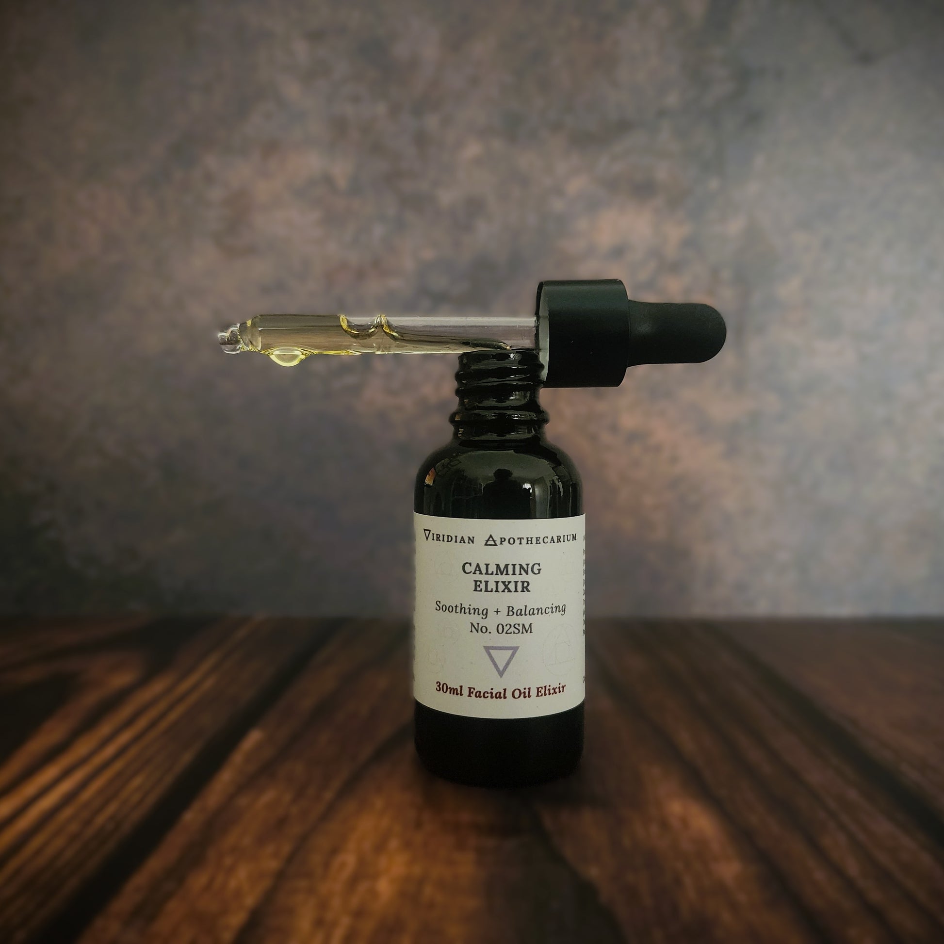 Bottle of 'Calming Elixir' by Viridian Apothecarium, with dropper on a wooden surface