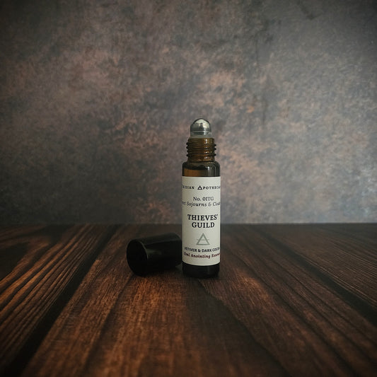 Thieves Guild essence Fragrance oil bottle on a wooden surface with a textured gray background. Viridian Apothecarium.