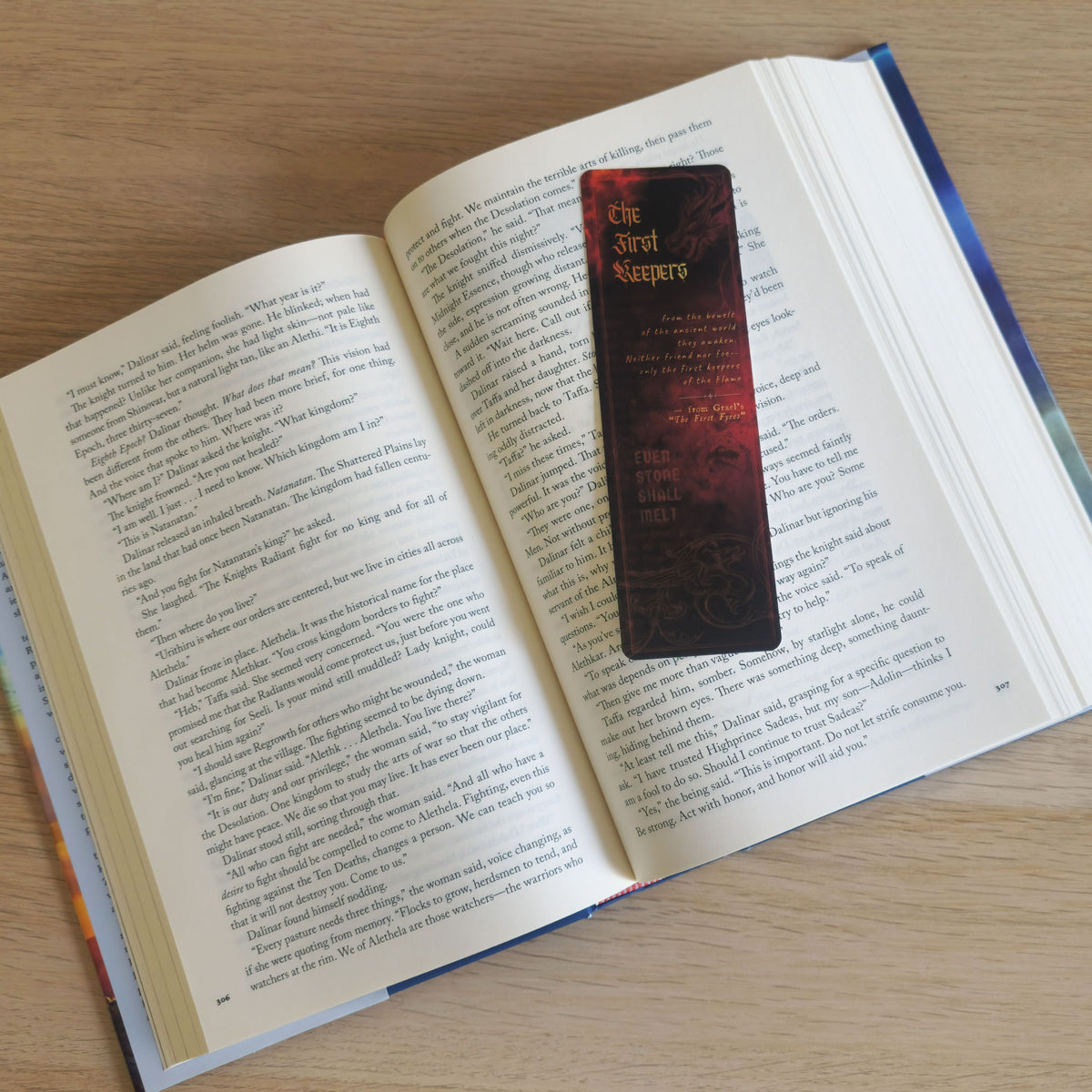 A dark red and black bookmark with gold lettering rests on the pages of an open book on a light wood surface.