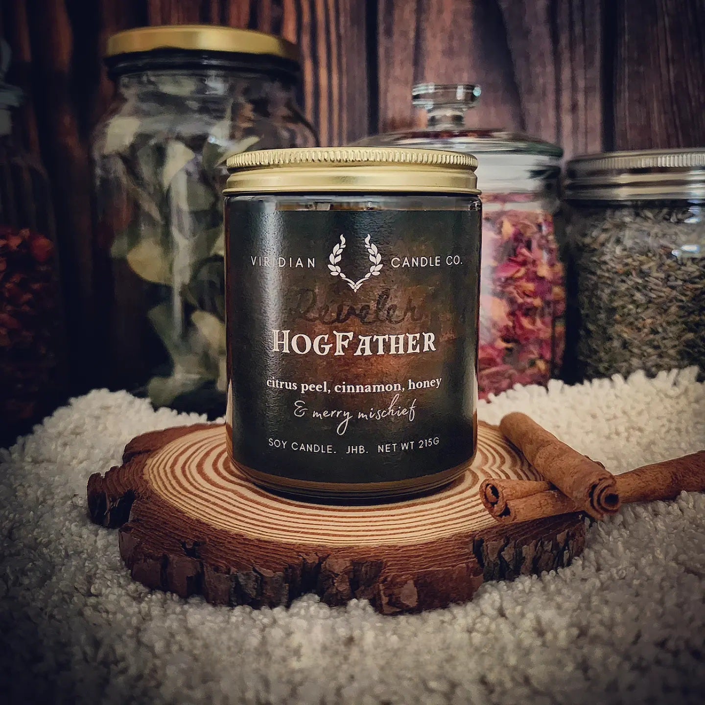 HogFather pure soy candle by Viridian Candle Co, inspired by Terry Pratchett, on an apothecary shelf with cinnamon quills, furs, dried botanicals - festive spiced citrus and plum notes
