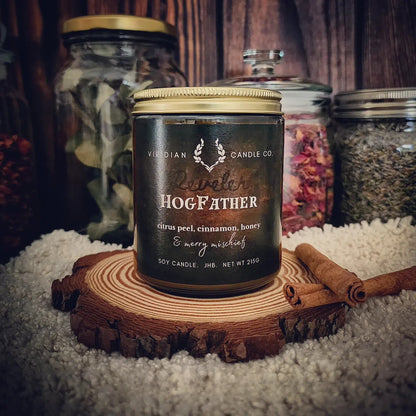 HogFather soy fantasy candle by Viridian Candle Co, inspired by Terry Pratchett, on an apothecary shelf with cinnamon quills, furs, dried botanicals - festive spiced citrus and plum notes