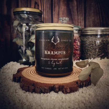Krampus soy fantasy candle by Viridian Candle Co, on an apothecary shelf with eucalyptus, furs, dried botanicals - dark Yuletide-inspired candle with citrus, spice, and woods