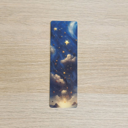A slim bookmark with rounded corners, featuring an artistic night sky design with blue clouds, glowing yellow stars, and a warm light at the bottom, placed on a light wood surface.