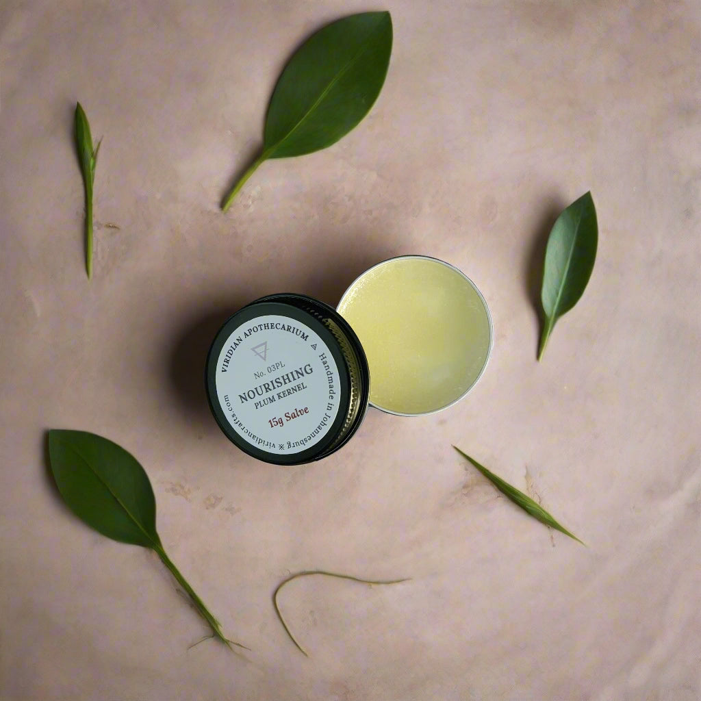 An opened tin of Nourishing Mini Salve by Viridian Apothecarium on a textured dark surface.
