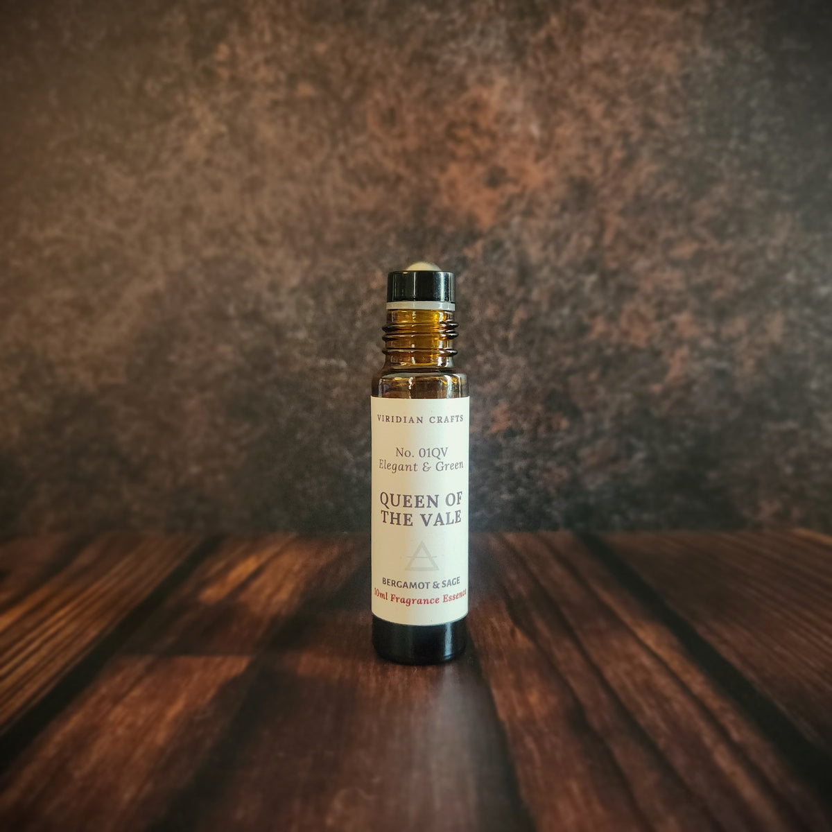 Queen of the Vale Essence - Perfume Roll-On 10ml amber bottle with bergamot and sage, handcrafted by Viridian Crafts on a moody industrial surface and background.