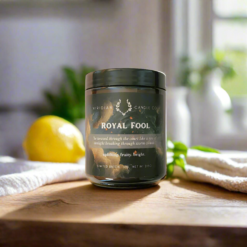 Royal Fool candle inspired by the fool archetype in fantasy books, handcrafted by Viridian Candle Co. on a kitchen table with warm sunlight.
