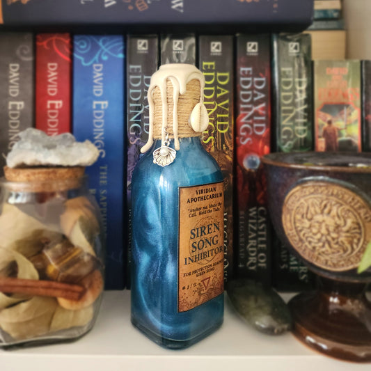 Bookshelf with books and a decorative bottle labeled 'Siren Song Inhibitor' on a white surface.