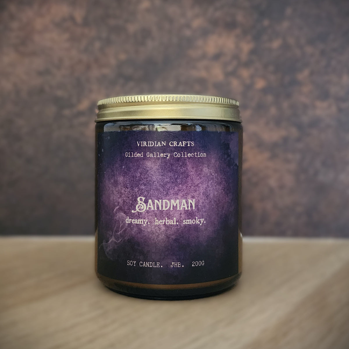 A jar candle with a purple watercolor-style label reading 'Sandman' and 'Viridian Crafts', set on a light wood surface against a textured brown background.