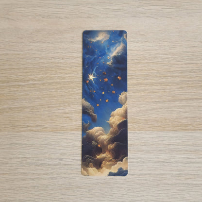 A slim rectangular book bookmark featuring a celestial night sky design with blue clouds, golden stars, and a bright shooting star, displayed on a light wood grain surface.